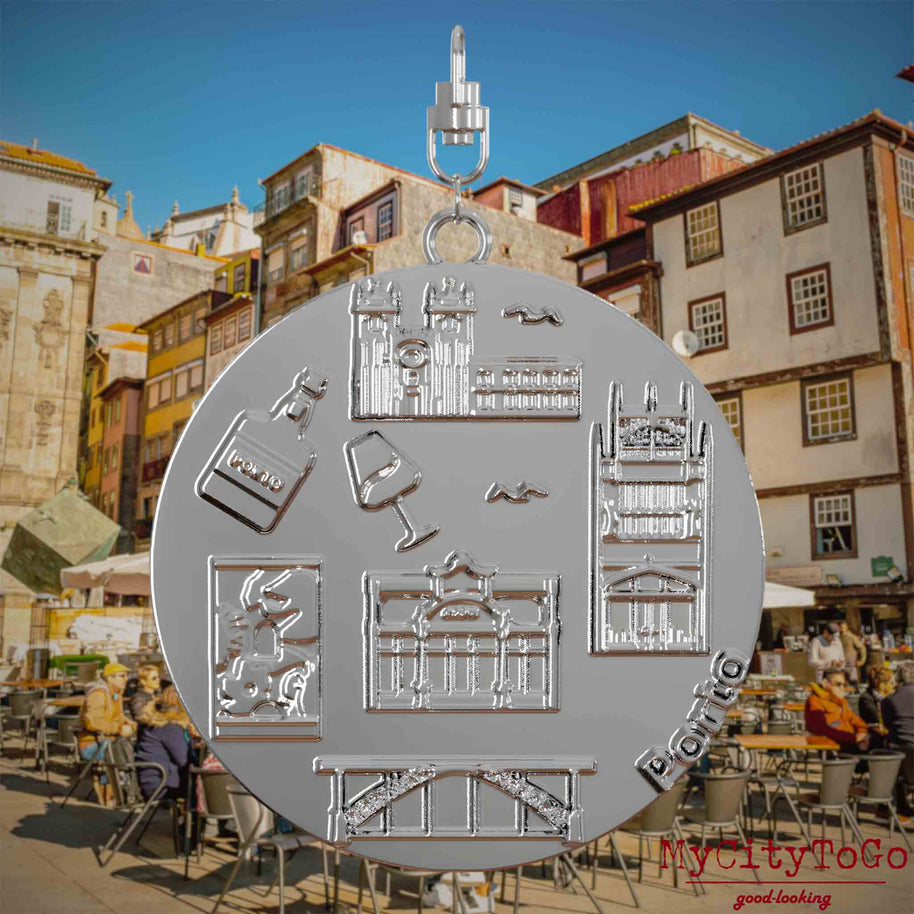 Halskette mit Drehwirbel und Rückseite eines silbernen Schmuckanhängers, auf dem Reliefs bekannter Sehenswürdigkeiten der Stadt Porto abgebildet sind. Den Hintergrund bildet eine Ansicht der Stadt Porto.
