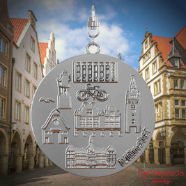 Halskette mit Drehwirbel und Rückseite eines silbernen Schmuckanhängers, auf dem Reliefs bekannter Sehenswürdigkeiten der Stadt Muenster abgebildet sind. Den Hintergrund bildet eine Ansicht der Stadt Muenster.