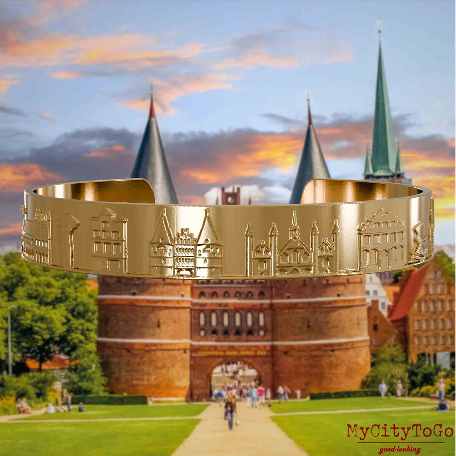 Vergoldeter Armreif mit Reliefs bekannter Sehenswürdigkeiten der Stadt Luebeck. Den Hintergrund bildet eine Ansicht der Stadt Luebeck.