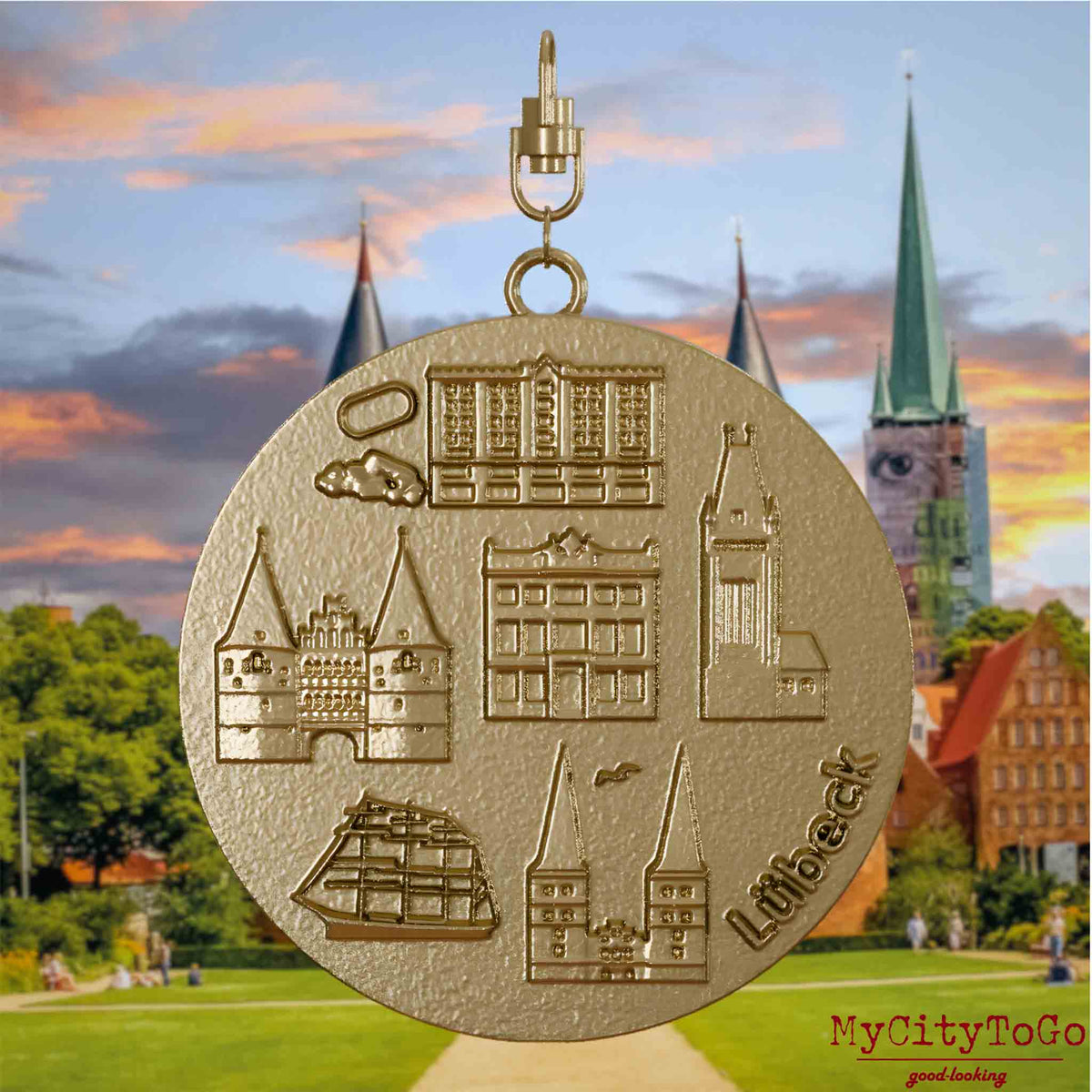 Halskette mit Drehwirbel und Rückseite eines Schmuckanhängers aus vergoldetem Edelstahl, auf dem Reliefs bekannter Sehenswürdigkeiten der Stadt Luebeck abgebildet sind. Den Hintergrund bildet eine Ansicht der Stadt Luebeck.
