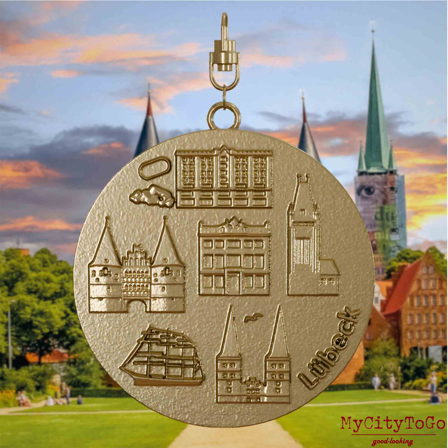 Halskette mit Drehwirbel und Rückseite eines Schmuckanhängers aus vergoldetem Edelstahl, auf dem Reliefs bekannter Sehenswürdigkeiten der Stadt Luebeck abgebildet sind. Den Hintergrund bildet eine Ansicht der Stadt Luebeck.
