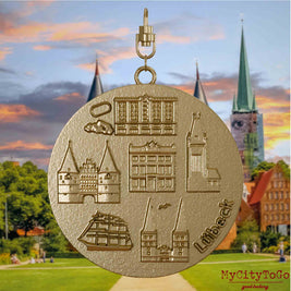 Halskette mit Drehwirbel und Rückseite eines Schmuckanhängers aus vergoldetem Edelstahl, auf dem Reliefs bekannter Sehenswürdigkeiten der Stadt Luebeck abgebildet sind. Den Hintergrund bildet eine Ansicht der Stadt Luebeck.
