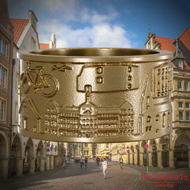 Ring aus vergoldetem Edelstahl mit Reliefs bekannter Sehenswürdigkeiten der Stadt Muenster. Den Hintergrund bildet eine Ansicht der Stadt Muenster.