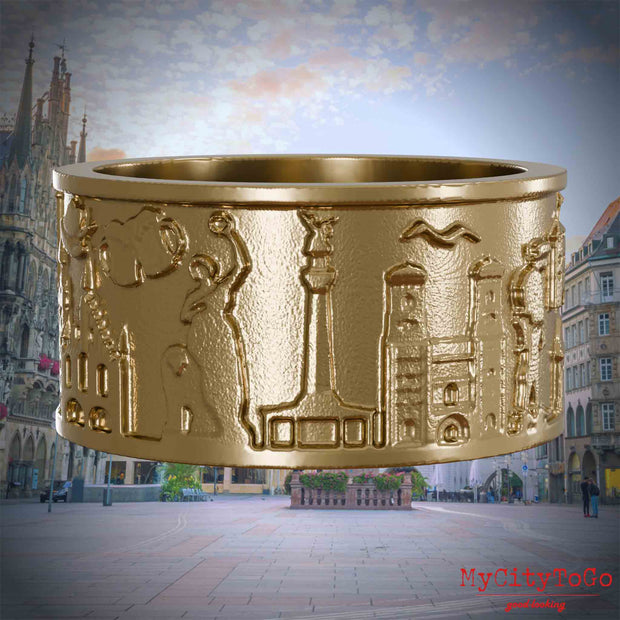 Ring aus vergoldetem Edelstahl mit Reliefs bekannter Sehenswürdigkeiten der Stadt Muenchen. Den Hintergrund bildet eine Ansicht der Stadt Muenchen.