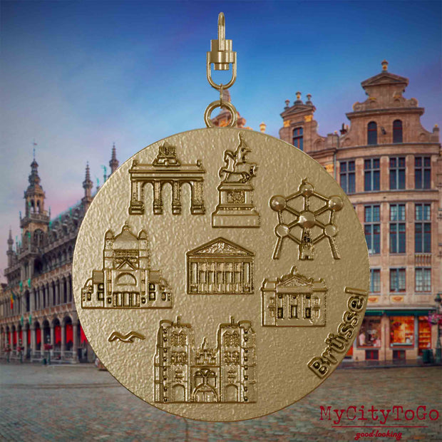 Halskette mit Drehwirbel und Rückseite eines Schmuckanhängers aus vergoldetem Edelstahl, auf dem Reliefs bekannter Sehenswürdigkeiten der Stadt Bruessel abgebildet sind. Den Hintergrund bildet eine Ansicht der Stadt Bruessel.
