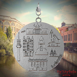 Halskette mit Drehwirbel und Vorderseite eines Schmuckanhänger , auf dem Reliefs bekannter Sehenswürdigkeiten der Stadt Leipzig abgebildet sind. Den Hintergrund bildet eine Ansicht der Stadt Leipzig.