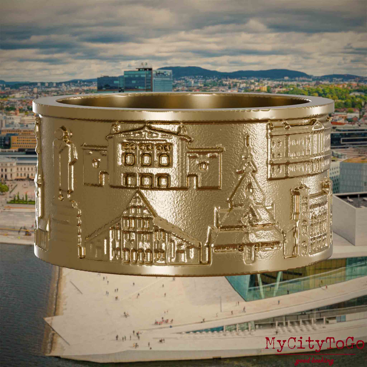 Ring aus vergoldetem Edelstahl mit Reliefs bekannter Sehenswürdigkeiten der Stadt Oslo. Den Hintergrund bildet eine Ansicht der Stadt Oslo.