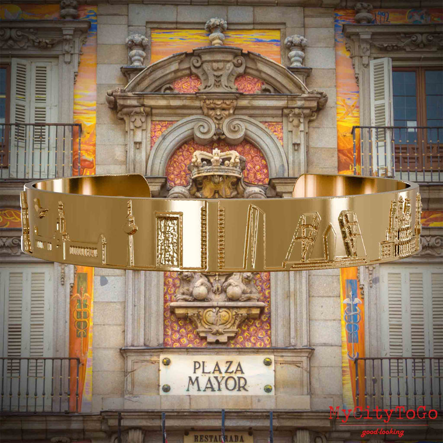 Vergoldeter Armreif mit Reliefs bekannter Sehenswürdigkeiten der Stadt Madrid. Den Hintergrund bildet eine Ansicht der Stadt Madrid.