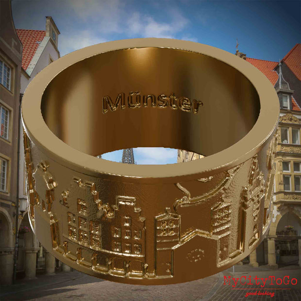 Ring aus vergoldetem Edelstahl mit Reliefs bekannter Sehenswürdigkeiten der Stadt Muenster und einer Gravur des Stadtnamens auf der Innenseite. Den Hintergrund bildet eine Ansicht der Stadt Muenster.