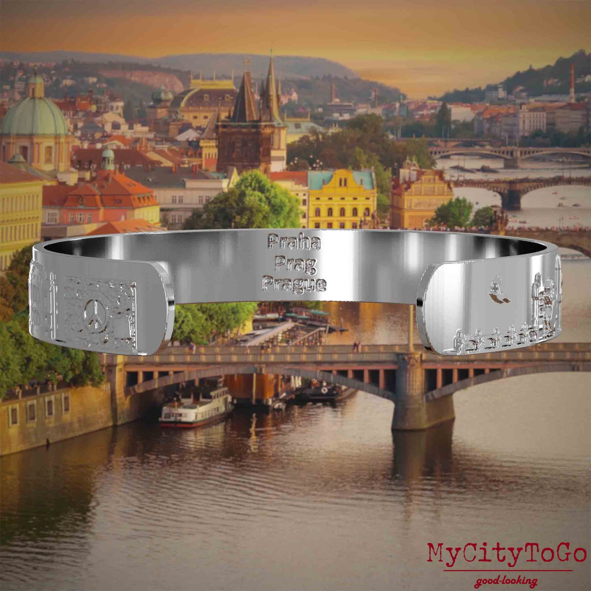 Innenseite eines silbernen Armreifs mit Reliefs bekannter Sehenswürdigkeiten der Stadt Prag und einer Gravur des Stadtnamens. Den Hintergrund bildet eine Ansicht der Stadt Prag.