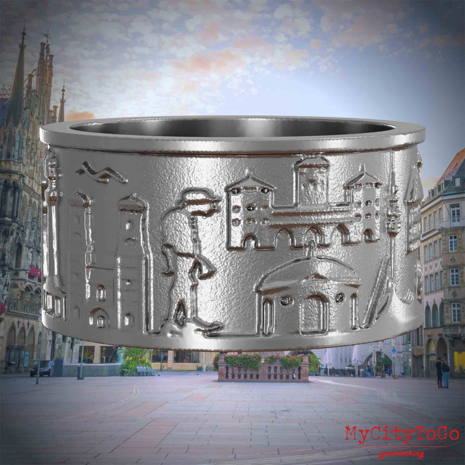 Ring aus Edelstahl mit Reliefs bekannter Sehenswürdigkeiten der Stadt Muenchen. Den Hintergrund bildet eine Ansicht der Stadt Muenchen.