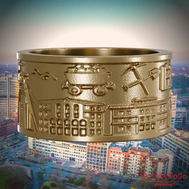 Ring aus vergoldetem Edelstahl mit Reliefs bekannter Sehenswürdigkeiten der Stadt Essen. Den Hintergrund bildet eine Ansicht der Stadt Essen.