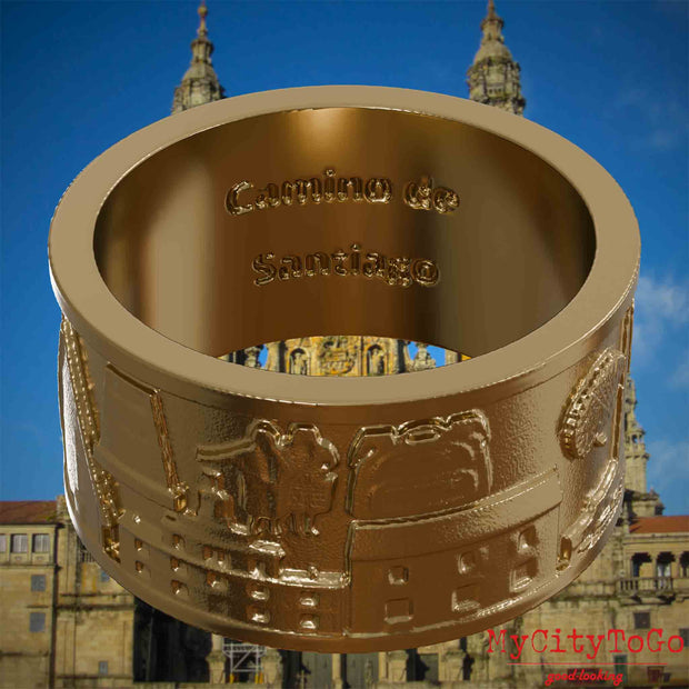 Ring aus vergoldetem Edelstahl mit Reliefs bekannter Sehenswürdigkeiten und Wahrzeichen auf dem Jakobsweg und der Gravur "Camino de Santiago" auf der Innenseite. Den Hintergrund bildet die Kathedrale von Santiago de Compostela.
