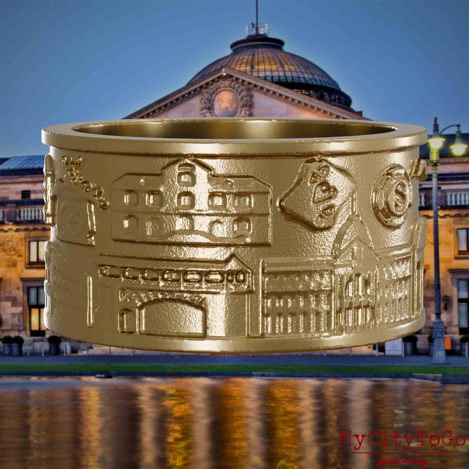 Ring aus vergoldetem Edelstahl mit Reliefs bekannter Sehenswürdigkeiten der Stadt Wiesbaden. Den Hintergrund bildet eine Ansicht der Stadt Wiesbaden. 