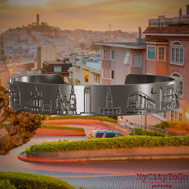 Armreif aus Titan mit Reliefs bekannter Sehenswürdigkeiten der Stadt San Francisco. Den Hintergrund bildet eine Ansicht der Stadt San Francisco.
