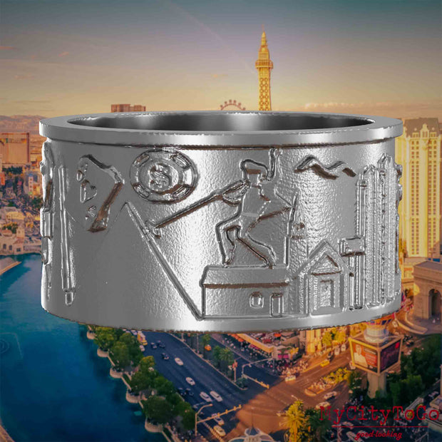 Ring aus Edelstahl mit Reliefs bekannter Sehenswürdigkeiten der Stadt Las Vegas. Den Hintergrund bildet eine Ansicht der Stadt Las Vegas.