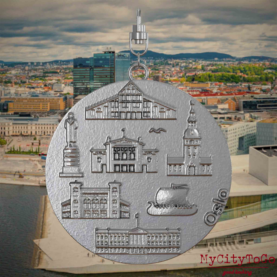 Halskette mit Drehwirbel und Rückseite eines Schmuckanhängers aus Edelstahl, auf dem Reliefs bekannter Sehenswürdigkeiten der Stadt Oslo abgebildet sind. Den Hintergrund bildet eine Ansicht der Stadt Oslo.
