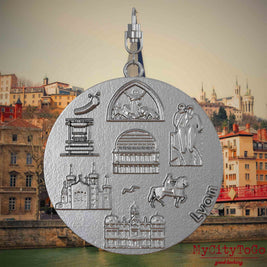 Halskette mit Drehwirbel und Rückseite eines Schmuckanhängers aus Edelstahl, auf dem Reliefs bekannter Sehenswürdigkeiten der Stadt Lyon abgebildet sind. Den Hintergrund bildet eine Ansicht der Stadt Lyon.
