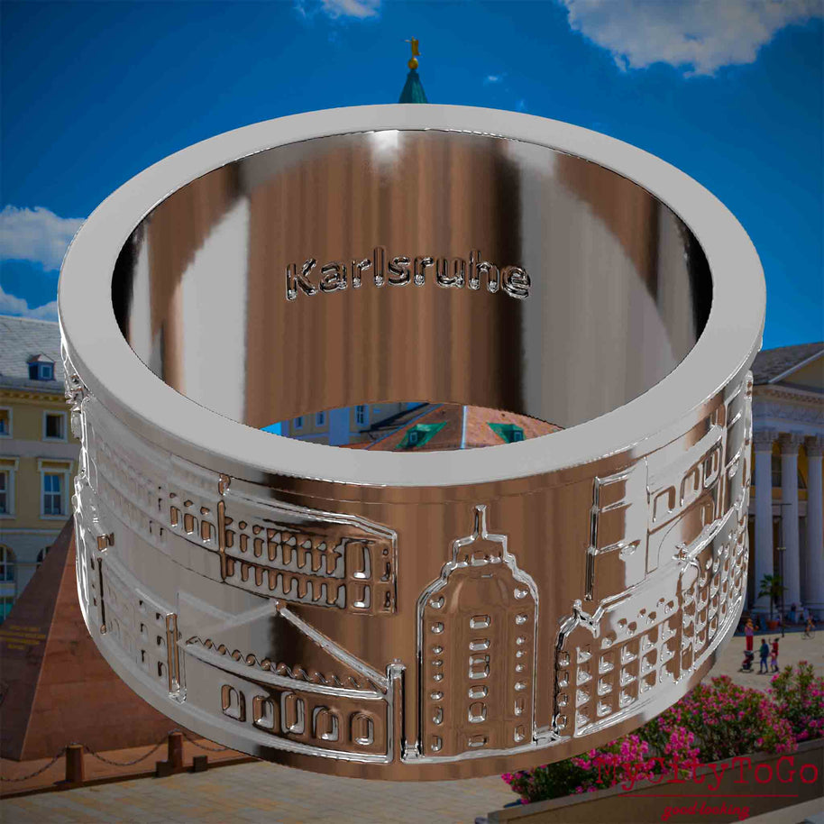 Versilberter Ring mit Reliefs bekannter Sehenswürdigkeiten der Stadt Karlsruheund einer Gravur des Stadtnamens auf der Innenseite. Den Hintergrund bildet eine Ansicht der Stadt Karlsruhe.