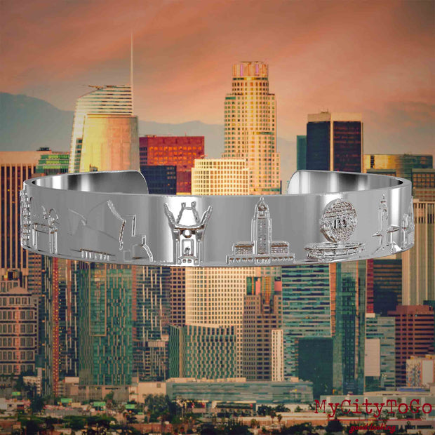 Versilberter Armreif mit Reliefs bekannter Sehenswürdigkeiten der Stadt Los Angeles. Den Hintergrund bildet eine Ansicht der Stadt Los Angeles.
