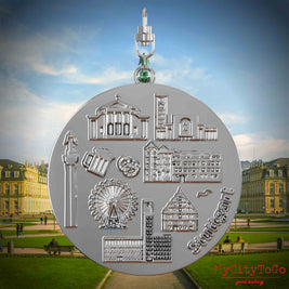 Halskette mit Drehwirbel und Rückseite eines silbernen Schmuckanhängers, auf dem Reliefs bekannter Sehenswürdigkeiten der Stadt Stuttgart abgebildet sind. Den Hintergrund bildet eine Ansicht der Stadt Stuttgart.

