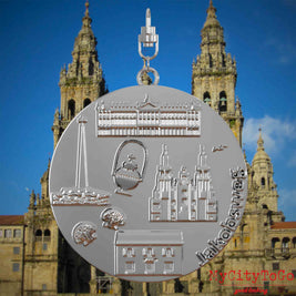 Halskette mit Drehwirbel und Rückseite eines silbernen Schmuckanhängers, auf dem Reliefs bekannter Sehenswürdigkeiten des Jakobwegs abgebildet sind. Den Hintergrund bildet eine Ansicht der Stadt Santiago de Compostela.
