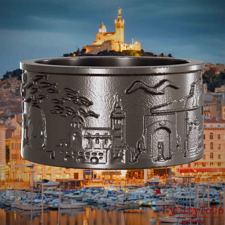 Ring aus Titan mit Reliefs bekannter Sehenswürdigkeiten der Stadt Marseille. Den Hintergrund bildet eine Ansicht der Stadt Marseille.