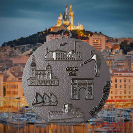 Halskette mit Drehwirbel und Vorderseite eines Schmuckanhängers aus Titan, auf dem Reliefs bekannter Sehenswürdigkeiten der Stadt Marseille abgebildet sind. Den Hintergrund bildet eine Ansicht der Stadt Marseille.
