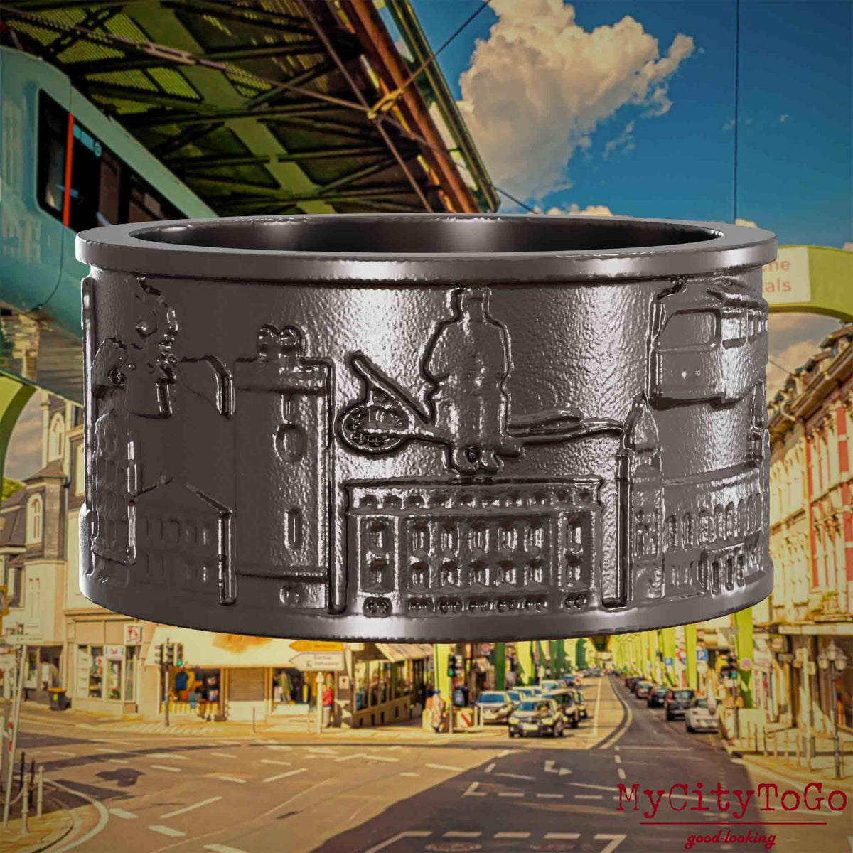 Ring aus Titan mit Reliefs bekannter Sehenswürdigkeiten der Stadt Wuppertal. Den Hintergrund bildet eine Ansicht  der Stadt Wuppertal.