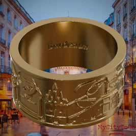 Ring aus vergoldetem Edelstahl mit Reliefs bekannter Sehenswürdigkeiten der Stadt Bordeaux und einer Gravur des Stadtnamens auf der Innenseite. Den Hintergrund bildet eine Ansicht der Stadt Bordeaux.