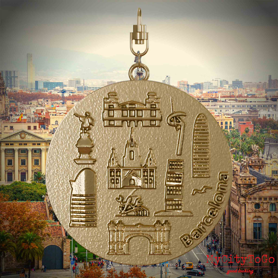 Halskette mit Drehwirbel und Vorderseite eines Schmuckanhängers aus vergoldetem Edelstahl, auf dem Reliefs bekannter Sehenswürdigkeiten der Stadt Barcelona abgebildet sind. Den Hintergrund bildet eine Ansicht der Stadt Barcelona.
