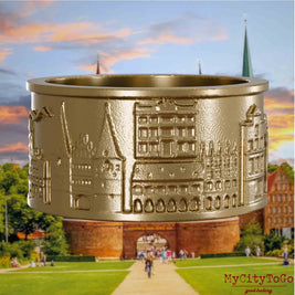 Ring aus vergoldetem Edelstahl mit Reliefs bekannter Sehenswürdigkeiten der Stadt Luebeck. Den Hintergrund bildet eine Ansicht der Stadt Luebeck.