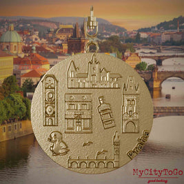 Halskette mit Drehwirbel und Vorderseite eines Schmuckanhängers aus vergoldetem Edelstahl, auf dem Reliefs bekannter Sehenswürdigkeiten der Stadt Prag abgebildet sind. Den Hintergrund bildet eine Ansicht der Stadt Prag.
