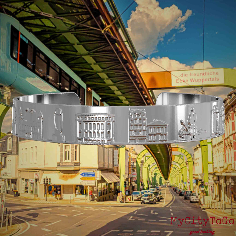 Versilberter Armreif mit Reliefs bekannter Sehenswürdigkeiten der Stadt Wuppertal. Den Hintergrund bildet eine Ansicht  der Stadt Wuppertal.