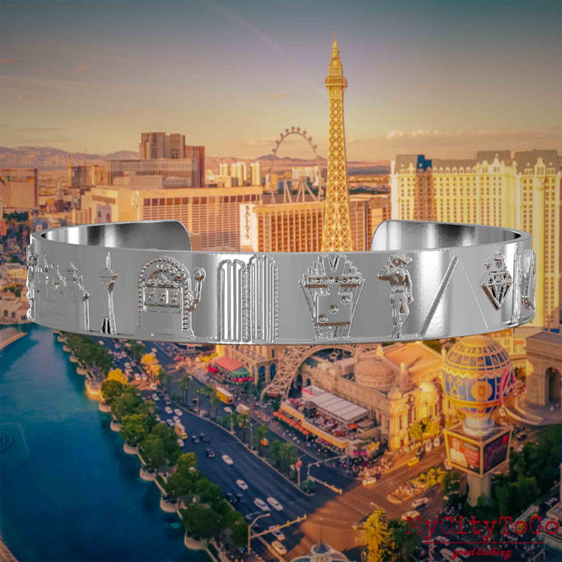 Versilberter Armreif mit Reliefs bekannter Sehenswürdigkeiten der Stadt Las Vegas. Den Hintergrund bildet eine Ansicht der Stadt Las Vegas.