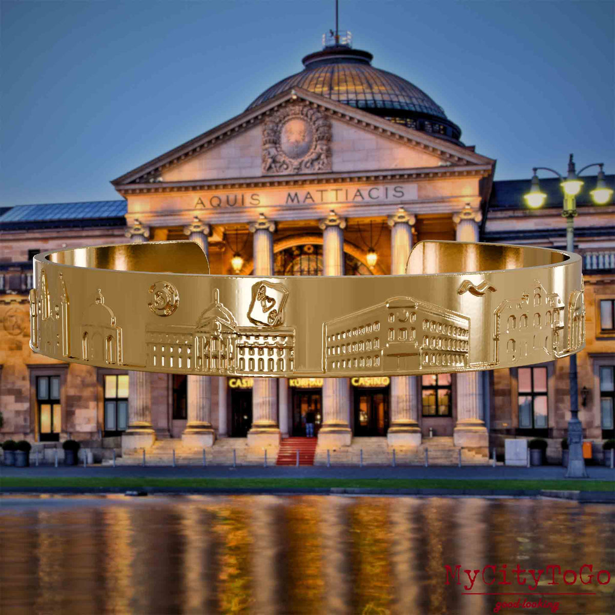 Vergoldeter Armreif mit Reliefs bekannter Sehenswürdigkeiten der Stadt Wiesbaden. Den Hintergrund bildet eine Ansicht der Stadt Wiesbaden.