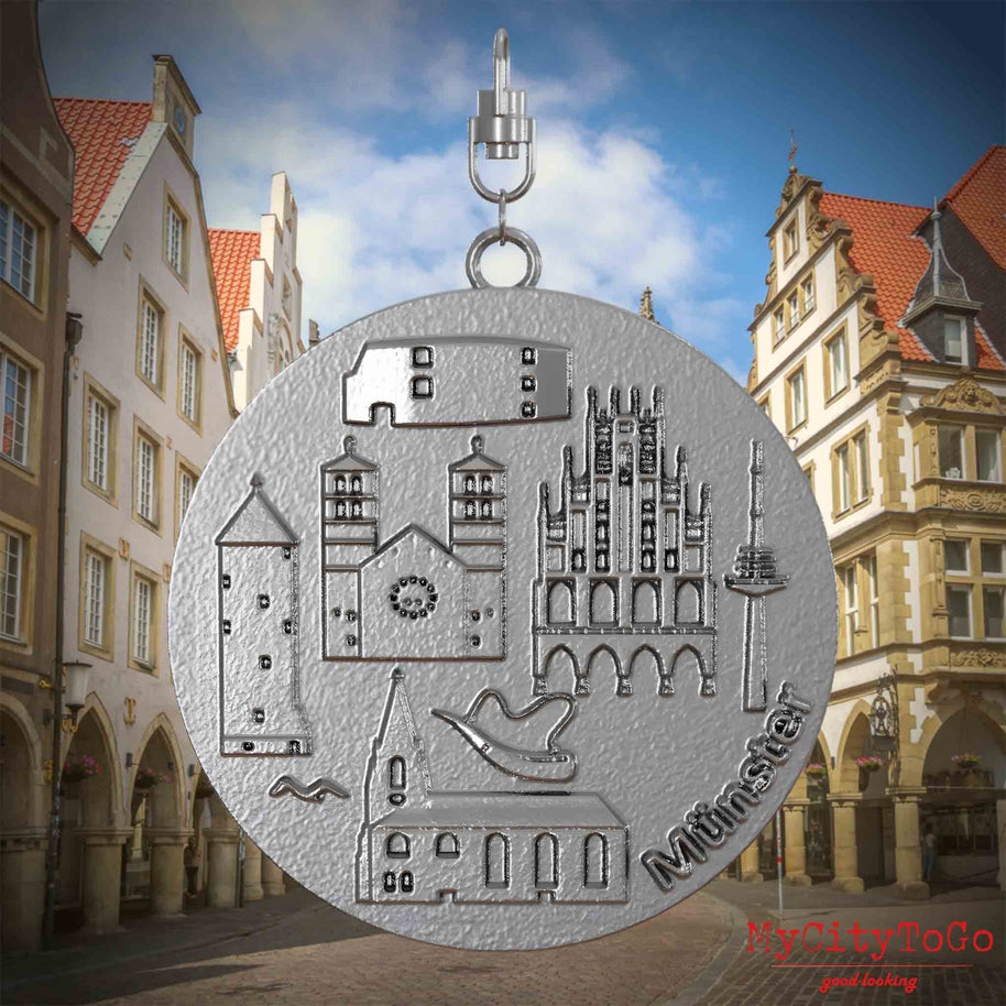 Halskette mit Drehwirbel und Vorderseite eines Schmuckanhängers aus Edelstahl, auf dem Reliefs bekannter Sehenswürdigkeiten der Stadt Muenster abgebildet sind. Den Hintergrund bildet eine Ansicht der Stadt Muenster.