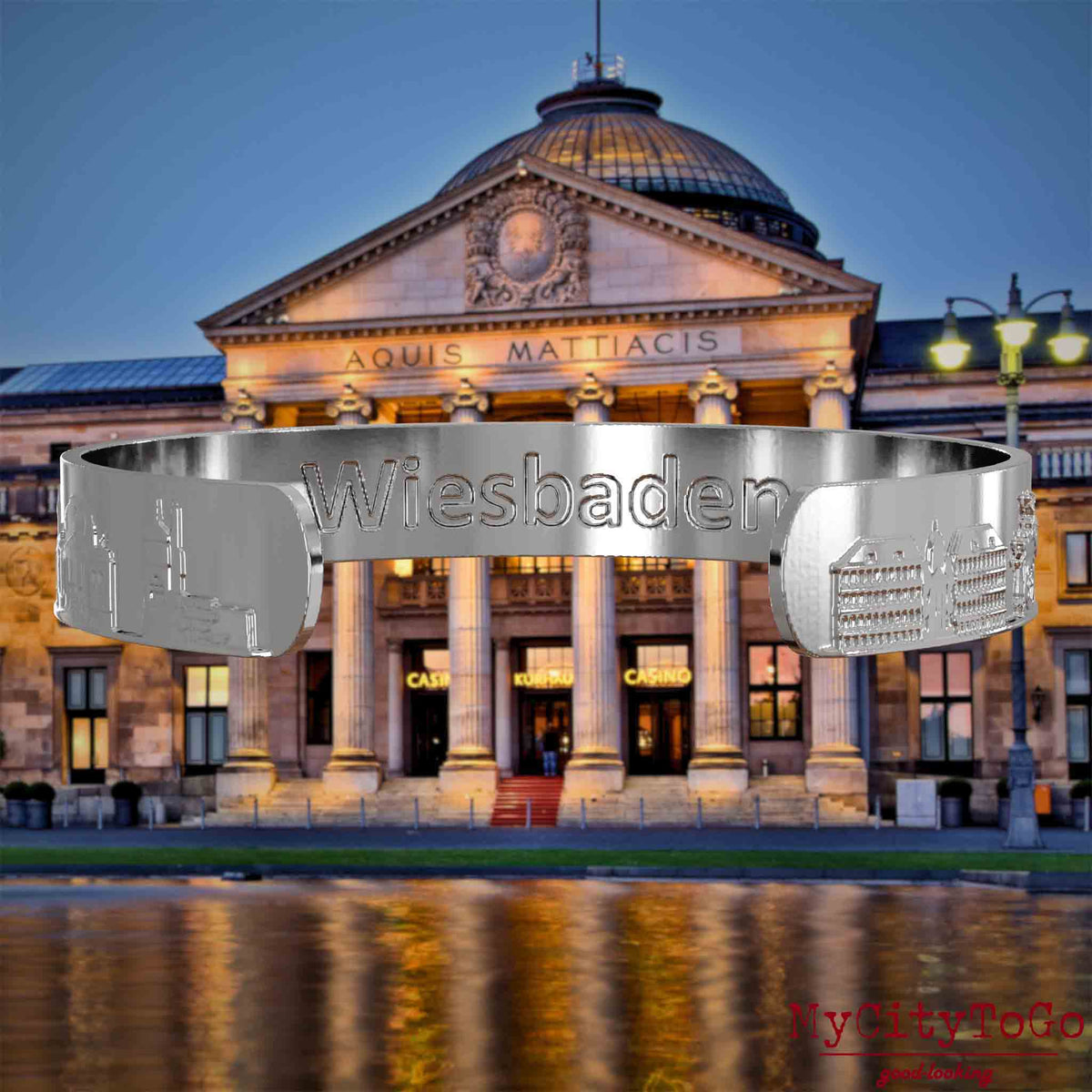 Innenseite eines silbernen Armreifs mit Reliefs bekannter Sehenswürdigkeiten der Stadt Wiesbaden und einer Gravur des Stadtnamens. Den Hintergrund bildet eine Ansicht der Stadt Wiesbaden.