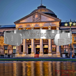 Innenseite eines silbernen Armreifs mit Reliefs bekannter Sehenswürdigkeiten der Stadt Wiesbaden und einer Gravur des Stadtnamens. Den Hintergrund bildet eine Ansicht der Stadt Wiesbaden.