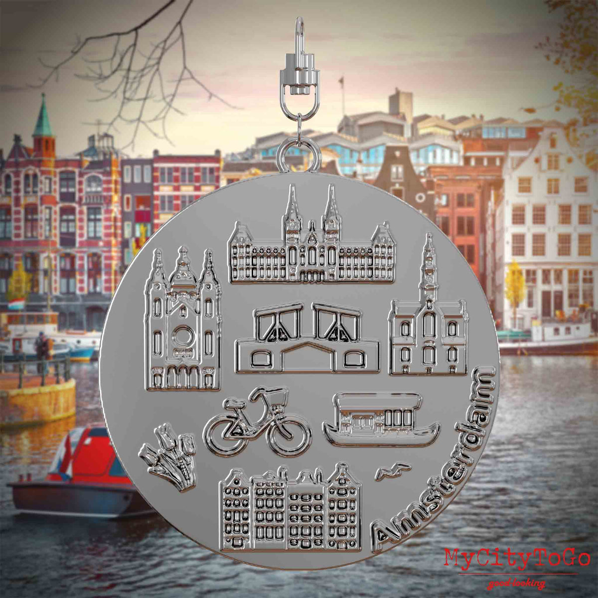 Halskette mit Drehwirbel und Vorderseite eines silbernen Schmuckanhängers, auf dem Reliefs bekannter Sehenswürdigkeiten der Stadt Amsterdam abgebildet sind. Den Hintergrund bildet eine Ansicht der Stadt Amsterdam.
