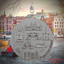 Halskette mit Drehwirbel und Vorderseite eines silbernen Schmuckanhängers, auf dem Reliefs bekannter Sehenswürdigkeiten der Stadt Amsterdam abgebildet sind. Den Hintergrund bildet eine Ansicht der Stadt Amsterdam.
