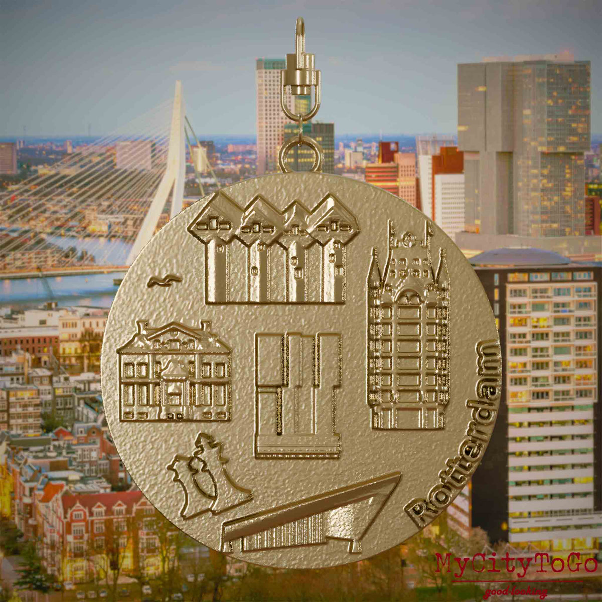 Halskette mit Drehwirbel und Vorderseite eines Schmuckanhängers aus vergoldetem Edelstahl, auf dem Reliefs bekannter Sehenswürdigkeiten der Stadt Rotterdam abgebildet sind. Den Hintergrund bildet eine Ansicht der Stadt Rotterdam.
