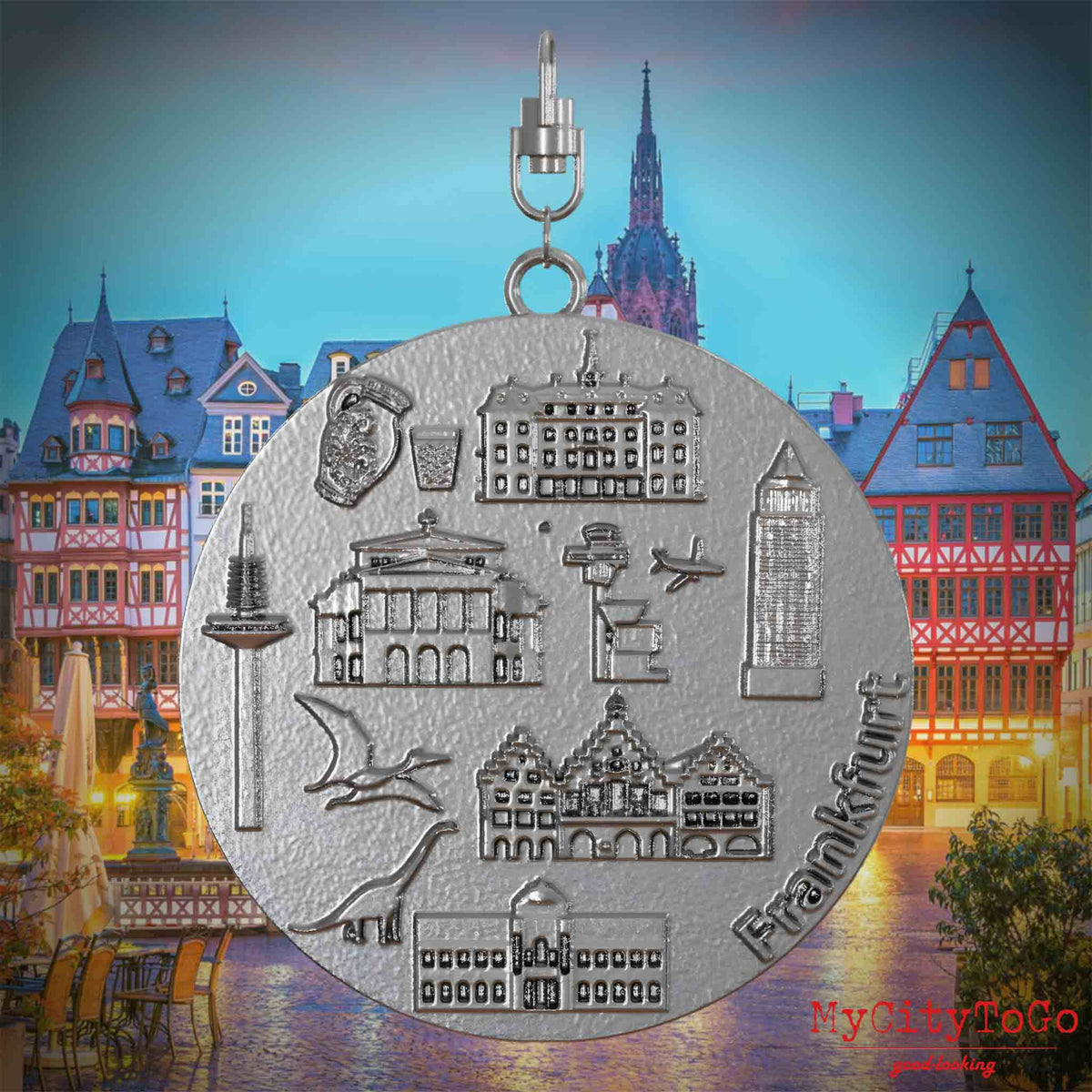 Halskette mit Drehwirbel und Rückseite eines Schmuckanhängers aus Edelstahl, auf dem Reliefs bekannter Sehenswürdigkeiten der Stadt Frankfurt abgebildet sind. Den Hintergrund bildet eine Ansicht der Stadt Frankfurt.