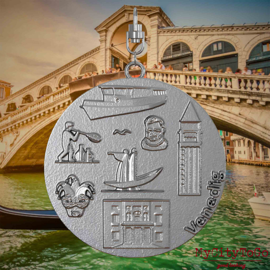 Halskette mit Drehwirbel und Rückseite eines Schmuckanhängers aus Edelstahl, auf dem Reliefs bekannter Sehenswürdigkeiten der Stadt Venedig abgebildet sind. Den Hintergrund bildet eine Ansicht der Stadt Venedig.
