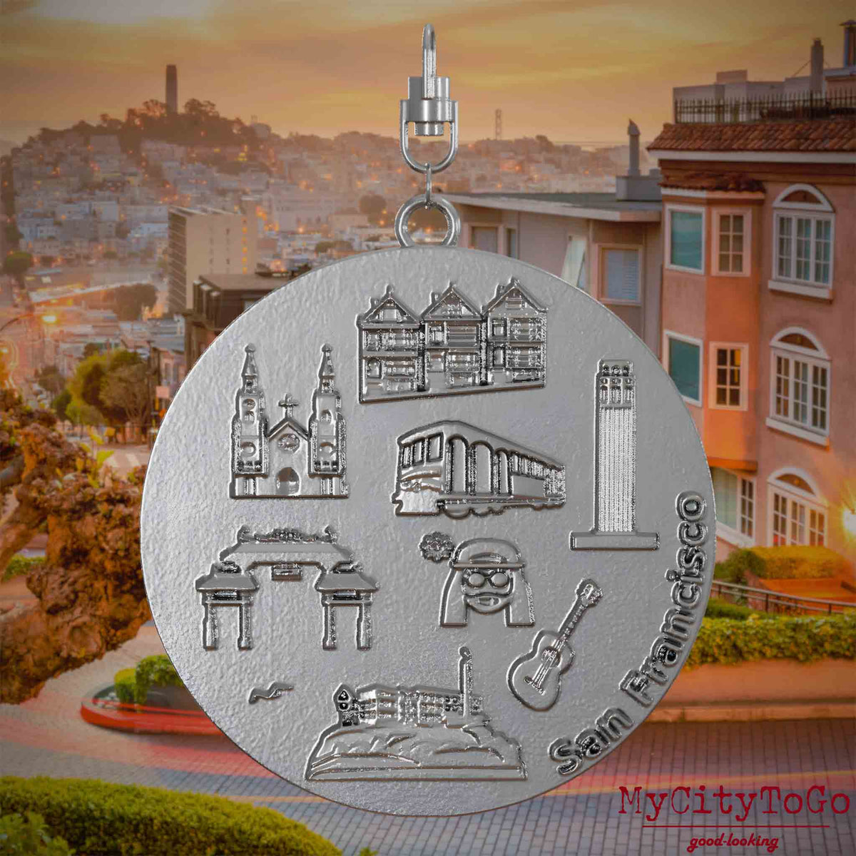 Halskette mit Drehwirbel und Rückseite eines Schmuckanhängers aus Edelstahl, auf dem Reliefs bekannter Sehenswürdigkeiten der Stadt San Francisco abgebildet sind. Den Hintergrund bildet eine Ansicht der Stadt San Francisco.
