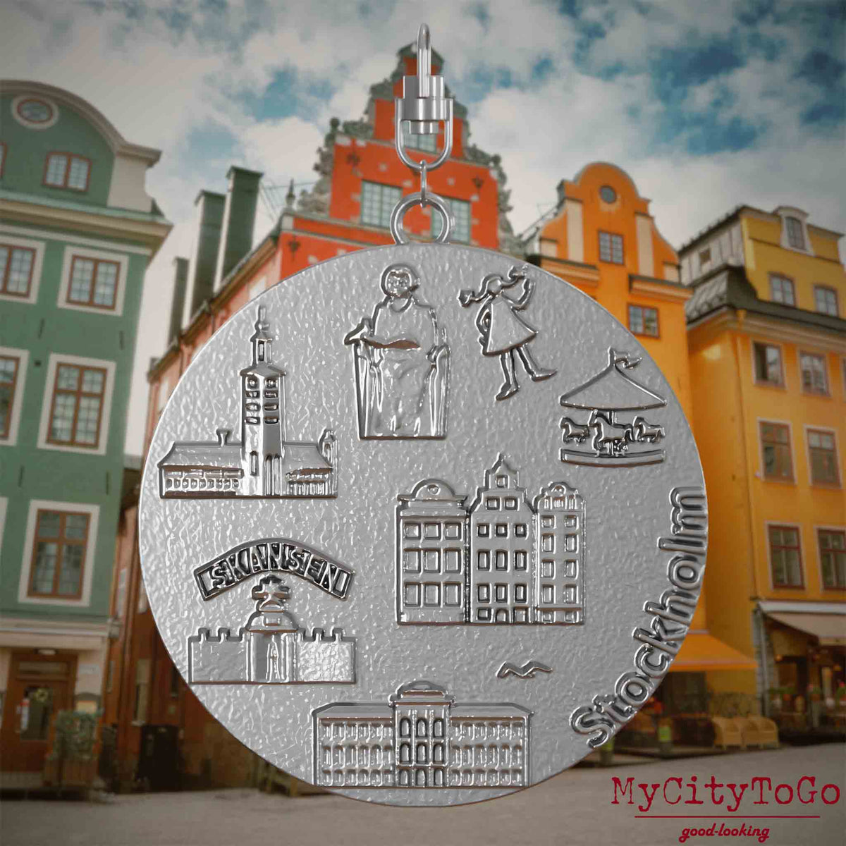 Halskette mit Drehwirbel und Rückseite eines Schmuckanhängers aus Edelstahl, auf dem Reliefs bekannter Sehenswürdigkeiten der Stadt Stockholm abgebildet sind. Den Hintergrund bildet eine Ansicht der Stadt Stockholm.
