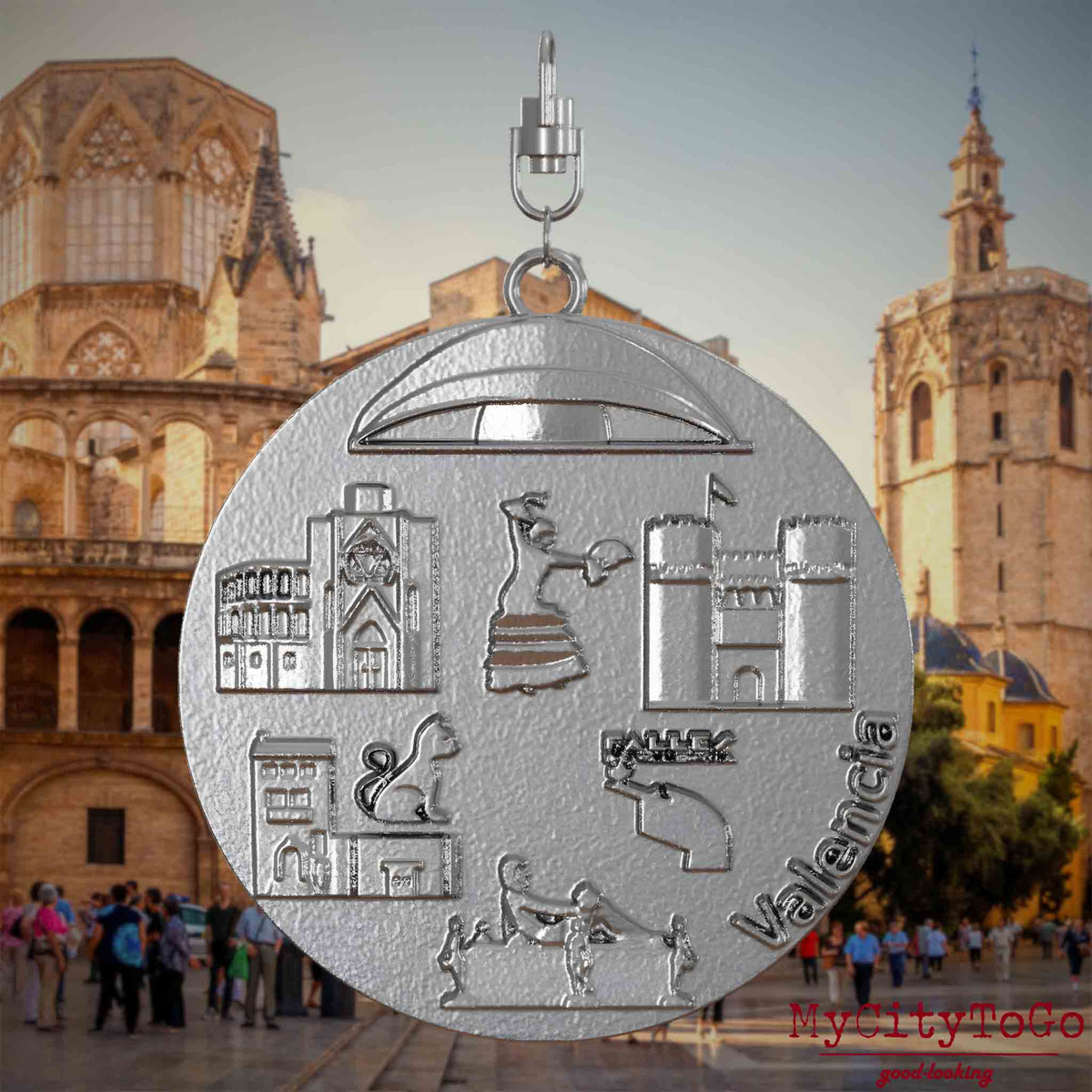 Halskette mit Drehwirbel und Rückseite eines Schmuckanhängers aus Edelstahl, auf dem Reliefs bekannter Sehenswürdigkeiten der Stadt Valencia abgebildet sind. Den Hintergrund bildet eine Ansicht der Stadt Valencia.
