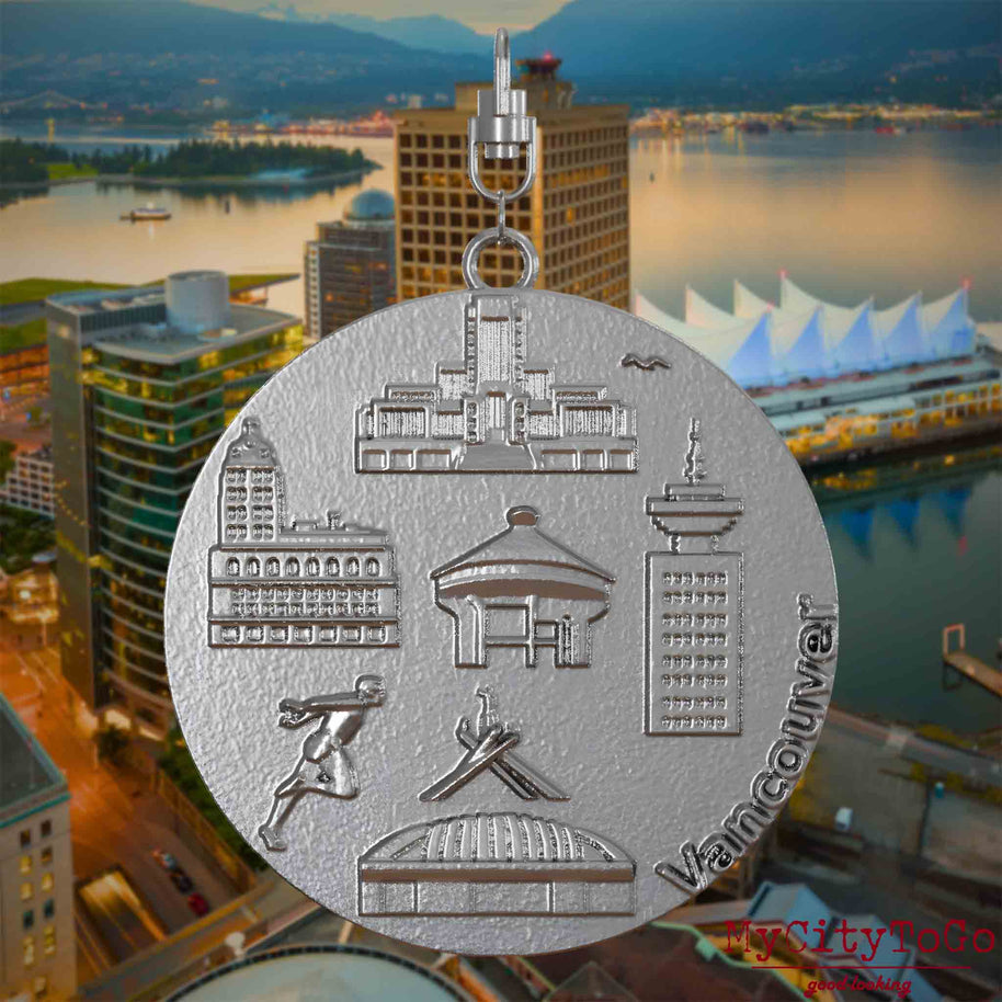 Halskette mit Drehwirbel und Rückseite eines Schmuckanhängers aus Edelstahl, auf dem Reliefs bekannter Sehenswürdigkeiten der Stadt Vancouver abgebildet sind. Den Hintergrund bildet eine Ansicht der Stadt Vancouver.
