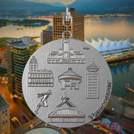 Halskette mit Drehwirbel und Rückseite eines Schmuckanhängers aus Edelstahl, auf dem Reliefs bekannter Sehenswürdigkeiten der Stadt Vancouver abgebildet sind. Den Hintergrund bildet eine Ansicht der Stadt Vancouver.
