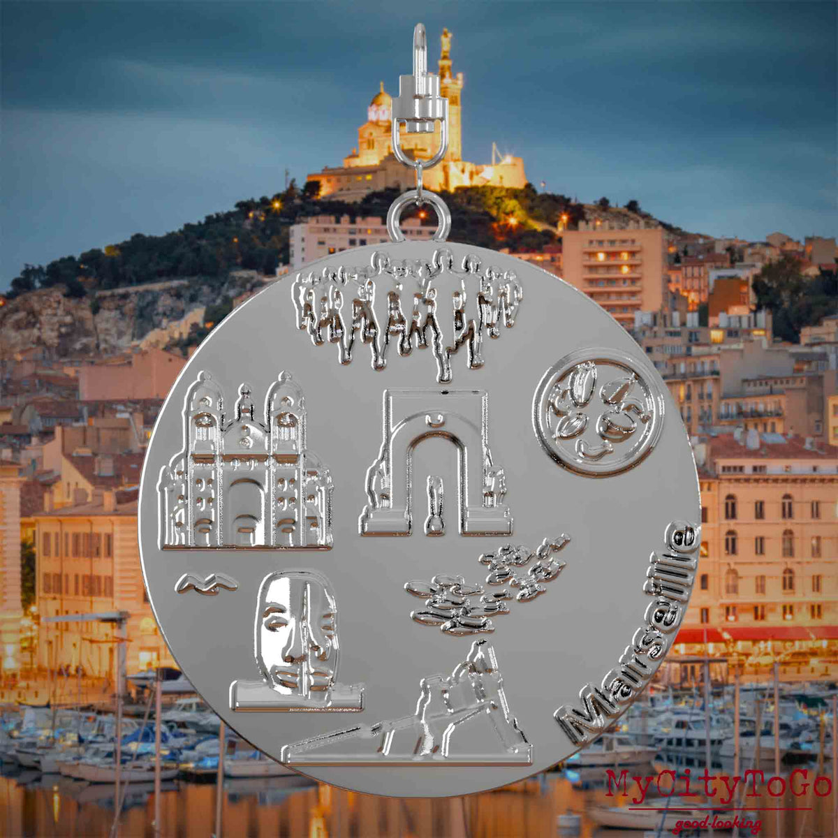 Halskette mit Drehwirbel und Rückseite eines silbernen Schmuckanhängers, auf dem Reliefs bekannter Sehenswürdigkeiten der Stadt Marseille abgebildet sind. Den Hintergrund bildet eine Ansicht der Stadt Marseille.
